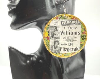 May include: A round, flat earring featuring a vintage-style collage print with yellow edges. The design displays black and white portraits of Cootie Williams and Ella Fitzgerald, along with text reading "Paradise," "2 Big Hits," and "In Person."