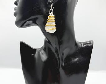May include: A drop earring featuring a white, irregularly shaped stone or clay piece wrapped in gold-colored wire. The earring hangs from a silver-toned metal hook. The piece has a textured, organic appearance with horizontal wire coils.