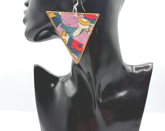May include: A triangular dangle earring featuring a colorful graphic pattern with shades of pink, blue, red, and yellow. The earring has a gold-toned border and is suspended from a silver-toned metal hook, displaying a vibrant, multi-colored design.