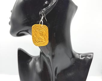 May include: A mustard yellow rectangular earring with a textured, concentric spiral pattern. The earring features a silver-toned metal hook for attachment, showcasing a distinct layered design that creates a tactile, raised surface appearance.