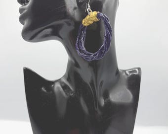 May include: A hoop earring featuring a circular design made of twisted dark purple cord. The top section of the hoop is wrapped in a metallic gold thread, and the earring is attached to a silver-toned metal hook for pierced ears.