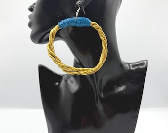 May include: A large hoop earring featuring a twisted metallic gold cord structure. The top section of the hoop is wrapped in a smooth, vibrant blue material. The earring is attached to a silver-toned metal hook for pierced ears.