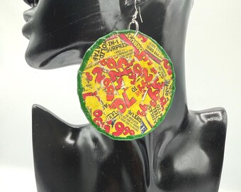 May include: A large, circular dangle earring featuring a collage of vintage-style yellow and red printed paper with bold numbers and text, finished with a green border and a silver-toned metal hook for attachment to the ear.