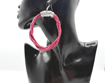 May include: A large hoop earring featuring a twisted, textured magenta cord material. The hoop is secured at the top by a decorative, embossed silver-toned metal connector piece, which attaches to a simple silver-toned metal ear wire hook.