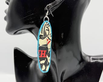 May include: A long, oval-shaped dangle earring featuring a graphic print with black, cream, and red elements, including a visible red letter H. The earring is edged in bright blue and hangs from a silver-toned metal hook wire.