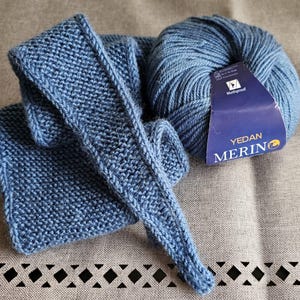 Op de afbeelding: Een blauwe gebreide sjaal en een bol blauwe wol met een label met de tekst "Yedan Merino" en "Mothproof".