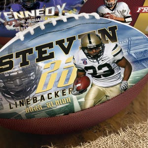 May include: A personalised American football with the name "STEVEN" in gold lettering. The image includes a football player in a white and gold uniform, the text "LINEBACKER" and "2023 SENIOR". The background shows a stadium.