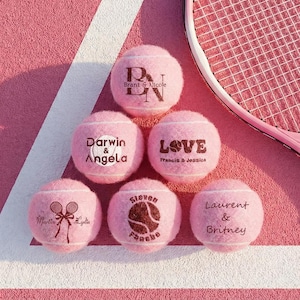 Puede incluir: Seis pelotas de tenis rosas dispuestas en triángulo, cada una con textos y gráficos personalizados que incluyen nombres como Brant & Nicole, Darwin & Angela, Francis & Jessica, Martin & Lydia, Steven Fesche y Laurent & Britney, junto a una raqueta.