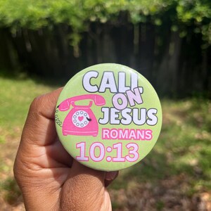 May include: A round, light green button with the text "CALL ON JESUS" in white and the word "ROMANS" in pink. A pink telephone graphic is featured above the text "10:13".