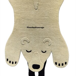 May include: A beige polar bear rug with a black nose, closed eyes, and black paw pads. The rug is held up by a person. The text "Floorfashionrugs" is visible on the rug.