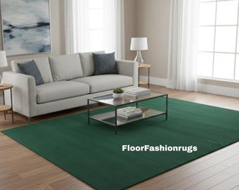 May include: A large, rectangular, emerald green rug dominates the foreground of a living room scene. A light gray sofa with blue accent pillows sits against a wall with a large abstract painting. A glass-topped coffee table and side tables with lamps complete the decor.