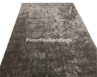 May include: A rectangular, gray rug with a textured surface. The rug has a mottled appearance with lighter and darker areas, creating a subtle pattern. The text "FloorFashionRugs" is visible on the rug.