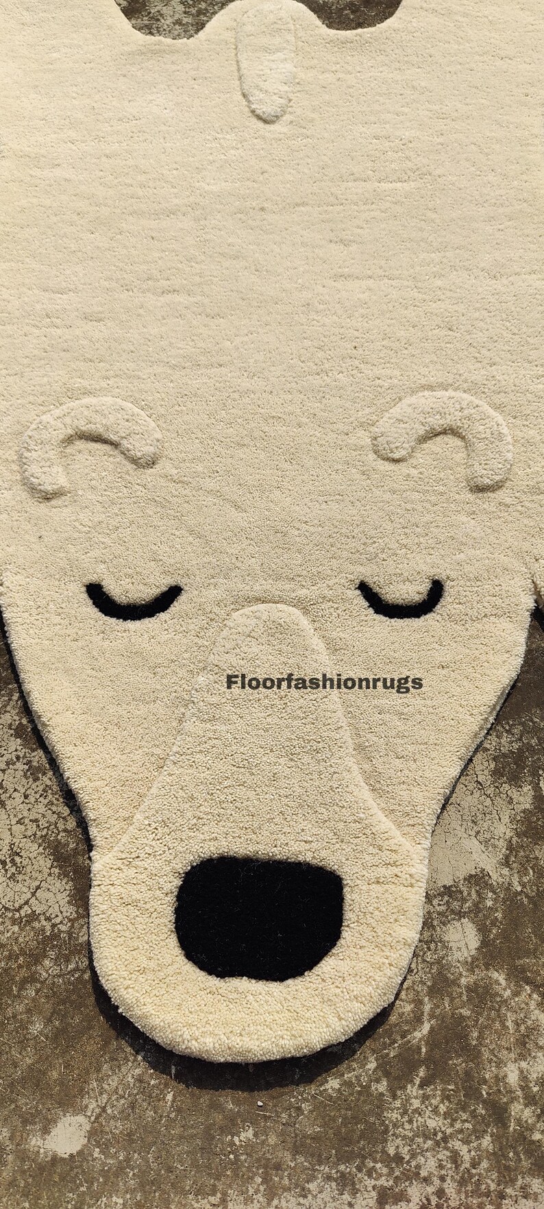 May include: A cream-colored rug shaped like a bear's face, featuring black eyes and a black open mouth. The rug has a textured surface and the text "Floorfashionrugs" is visible. This rug is suitable for a child's room or nursery.