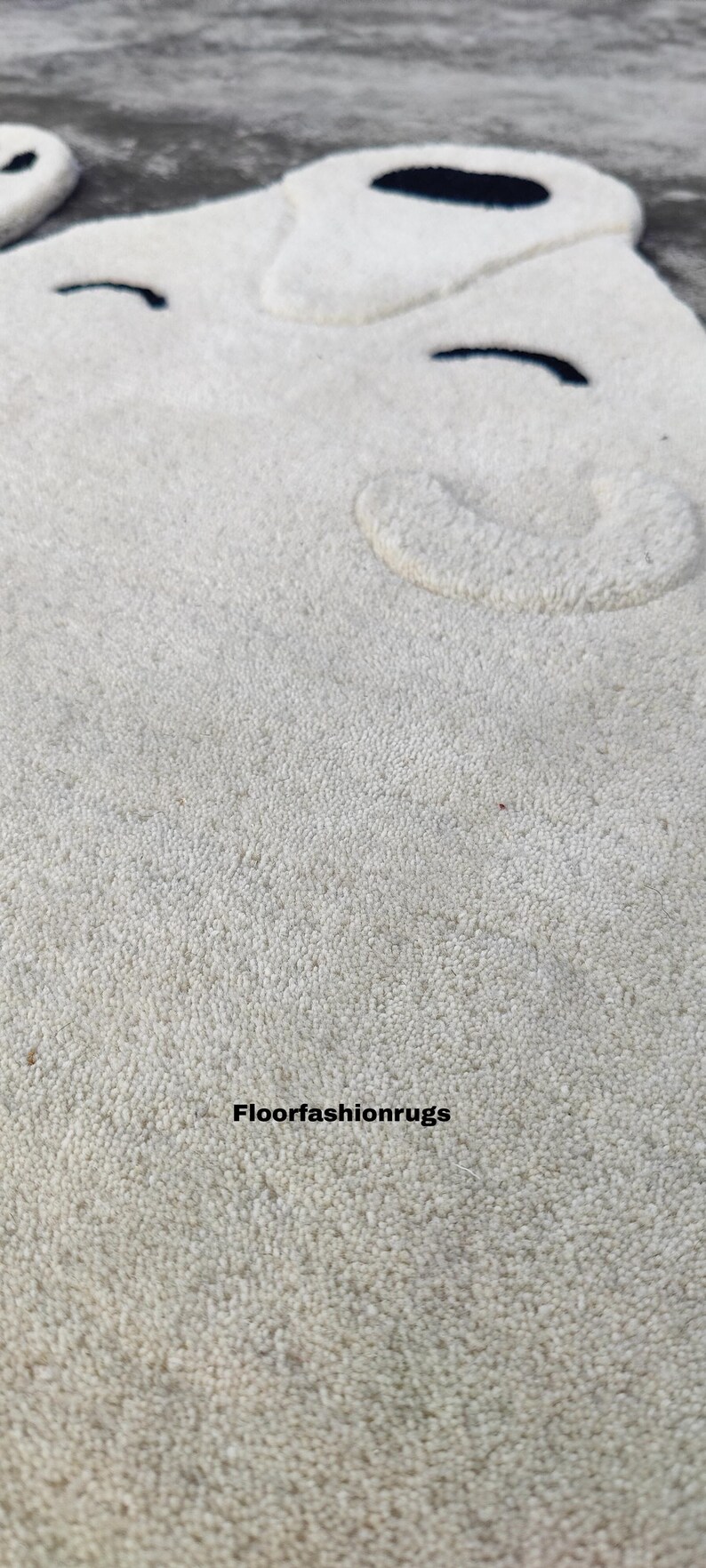 May include: A cream-colored rug with a textured surface and a bear-shaped design. The rug features a bear face with black eyes and a rounded ear. The text "Floorfashionrugs" is at the bottom.