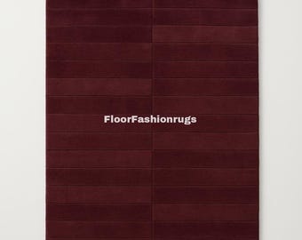 May include: A rectangular burgundy rug with a textured, segmented design. The rug is divided into horizontal sections, creating a ribbed appearance. The text "FloorFashionrugs" is displayed in white.