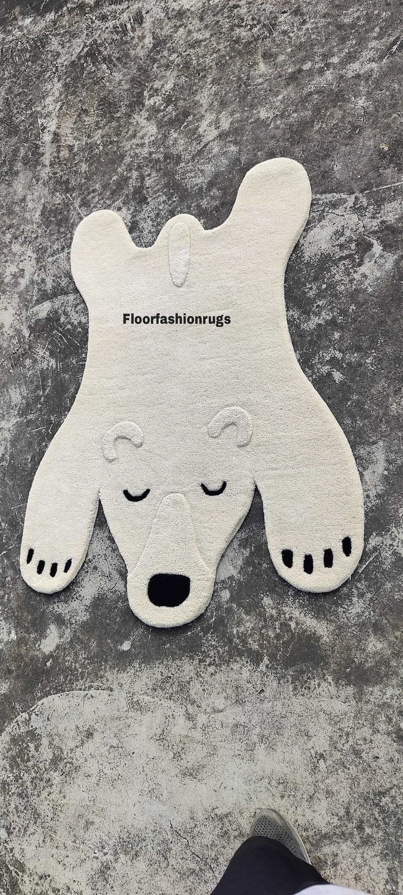 May include: A cream-colored polar bear rug with a black nose, closed eyes, and paw pads. The rug has a soft, textured appearance and is shaped like a bear. The text "Floorfashionrugs" is visible on the rug.