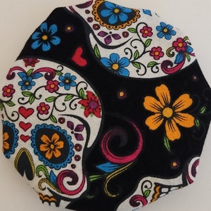 May include: A black fabric with a white sugar skull design. The skull is decorated with colorful flowers, hearts, and swirls.