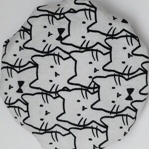 May include: White fabric with a repeating pattern of black cat faces. The cats have simple features, including eyes, a nose, and whiskers.