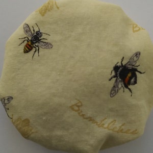 May include: A light yellow fabric bee-themed reusable food wrap with the word "Bumblebee" printed on it. The wrap features a black and yellow bumblebee and a yellow and black bee.
