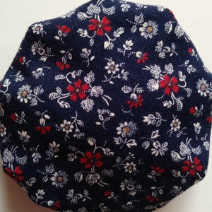 May include: A close-up of a dark blue fabric with a white and red floral pattern. The fabric is textured and has a subtle sheen.