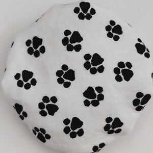 May include: White fabric with a black paw print pattern. The fabric is round and appears to be a shower cap.