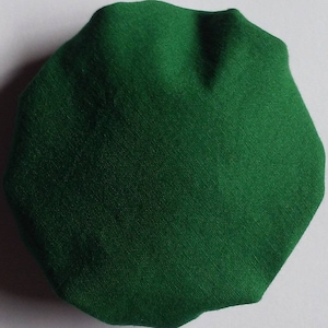 May include: A solid green, irregularly shaped fabric item. The item has a textured surface and appears to be made of a woven material. The shape is reminiscent of a polygon with rounded edges. The color is a deep, vibrant green.