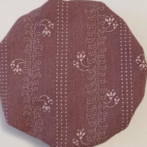 May include: A close-up of a mauve fabric with a white floral pattern and white polka dots. The fabric is textured and has a slightly rough feel.