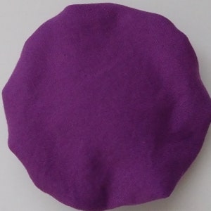 May include: A solid purple, round fabric item with a slightly irregular edge. The fabric has a textured appearance, suggesting a woven material. The color is a vibrant, saturated shade of purple.