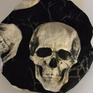 May include: Black fabric with a white skull pattern. The skull has a detailed design with eye sockets, a nose, and a mouth.