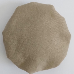 May include: A circular, tan-colored fabric cap with a gathered, elasticized edge. The material features a visible, fine-woven texture throughout the surface, creating a soft, rounded shape that is uniform in color and design across the entire item.