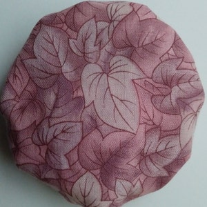 May include: A round, pink fabric with a leaf pattern. The leaves are a darker shade of pink and are outlined in a darker shade of pink.
