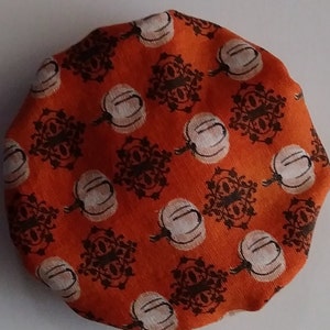 May include: Orange fabric with a repeating pattern of white pumpkins and brown stylized floral designs.