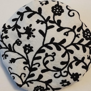 May include: White fabric circle with a black floral pattern. The pattern features stylized flowers and leaves.