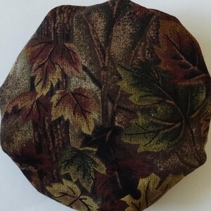 May include: A round fabric with a brown, green, and yellow leaf pattern. The fabric has a textured surface.