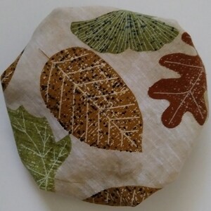 May include: A beige fabric with a pattern of brown, green, and orange leaves. The leaves are stylized and have a textured look.