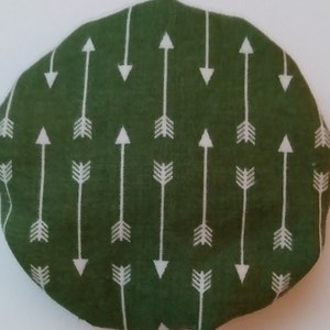 May include: A round, green fabric item with a repeating pattern of white arrows pointing up and down. The arrows have a simple, geometric design, and the fabric has a slightly textured appearance.