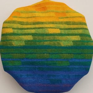 May include: A round, fabric-covered, colorful, striped, decorative object with a rainbow pattern. The colors are yellow, green, blue, and purple.