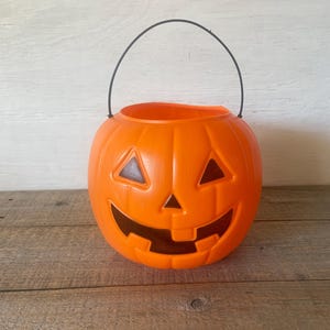 May include: Orange plastic pumpkin shaped Halloween trick or treat bucket with a black handle.
