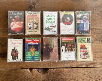 May include: A collection of ten vintage cassette tapes featuring various country Christmas music artists. The tapes are arranged in two rows of five on a wooden surface. The titles of the tapes include "Country Christmas", "Marty Willie Mickey", "Christmas in Nashville", "Christmas Rock", "The Christmas Album Gladys Knight & The Pips", "A Country Christmas", "Lee Greenwood Country Christmas", "Christmas Favorites Ronnie Milsap The Judds", and "A Country Christmas".