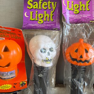 May include: Halloween-themed decorative lights, including an orange pumpkin light and a white skull light, packaged in plastic. The packaging includes the words "Safety Light" and "Halloween Pumpkin Light".