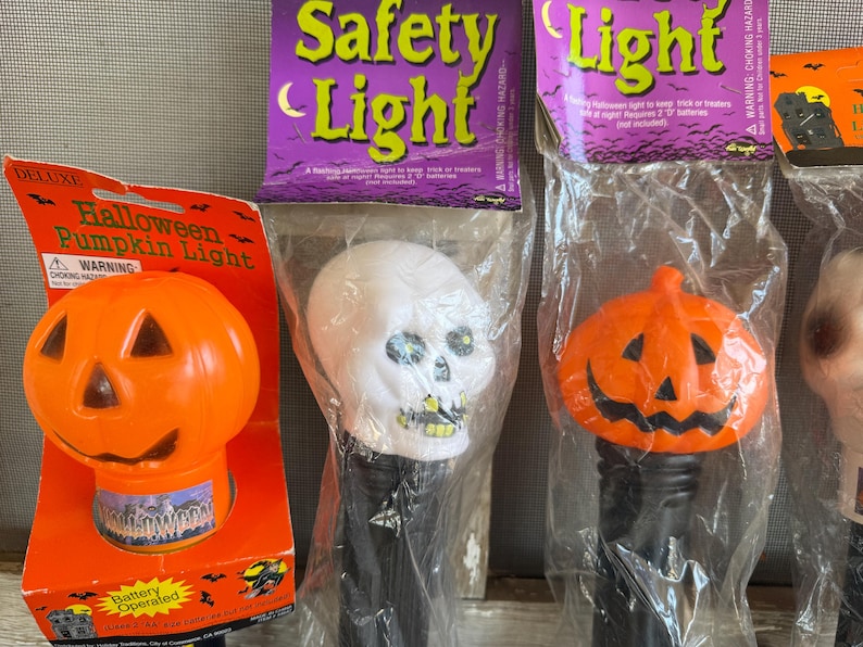May include: Halloween-themed decorative lights, including an orange pumpkin light and a white skull light, packaged in plastic. The packaging includes the words "Safety Light" and "Halloween Pumpkin Light".