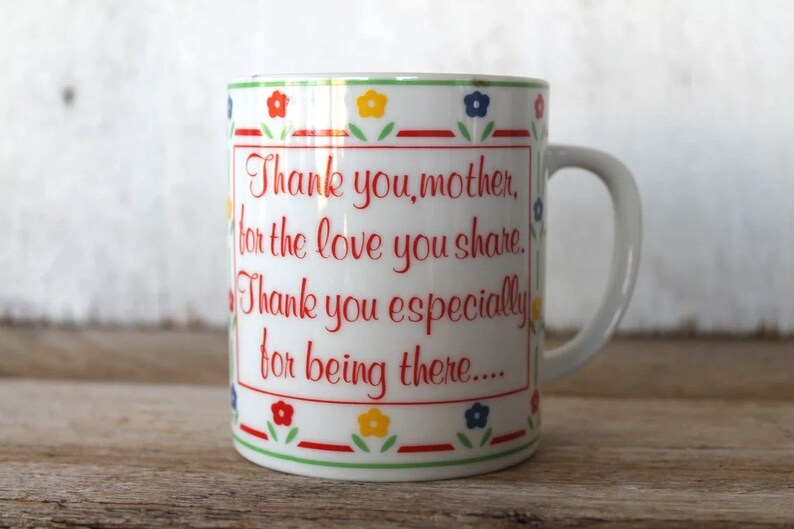 K&ouml;nnte beinhalten: Wei&szlig;e Keramiktasse mit einem roten, gr&uuml;nen, blauen und gelben Blumendesign. Die Tasse hat einen Henkel und sagt "Danke, Mutter, f&uuml;r die Liebe, die du teilst. Danke besonders daf&uuml;r, dass du da bist..."