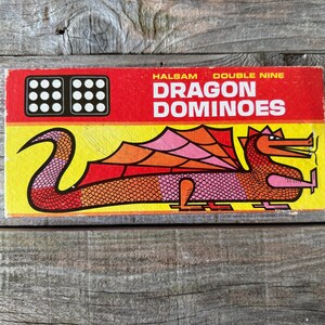 May include: Vintage "Dragon Dominoes" game box. The box is red and yellow with a dragon illustration in orange, pink, and red. The text "DRAGON DOMINOES" is in white letters. The box also has two sets of domino dots.