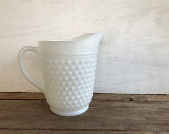 May include: White milk glass pitcher with a textured, raised dot pattern. The pitcher has a handle and a wide mouth.