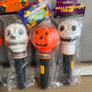 May include: Halloween-themed light-up flashlights and a light-up stick. The flashlights are shaped like a skull and a pumpkin. The flashlights are black and white with the text "Halloween" on the base. The packaging reads "Halloween Pumpkin LIGHT-UP FLASHLIGHT".