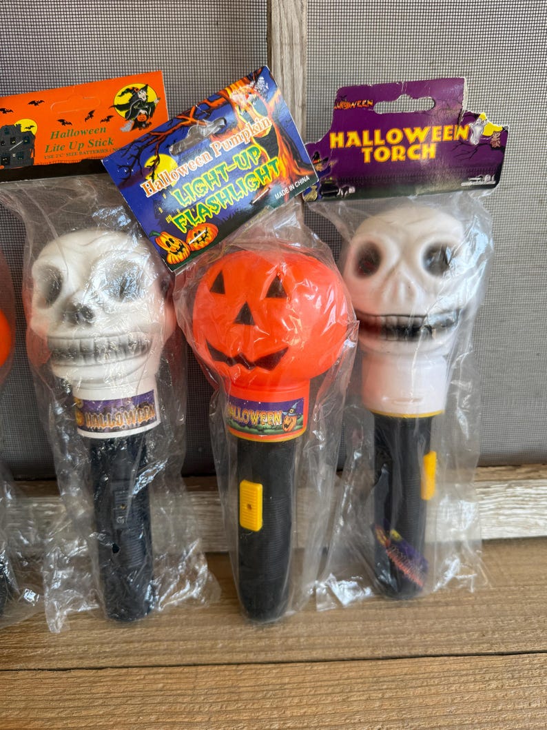 May include: Halloween-themed light-up flashlights and a light-up stick. The flashlights are shaped like a skull and a pumpkin. The flashlights are black and white with the text "Halloween" on the base. The packaging reads "Halloween Pumpkin LIGHT-UP FLASHLIGHT".