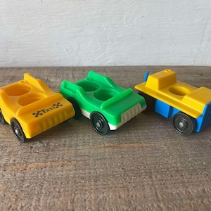 Könnte beinhalten: Drei Vintage-Spielzeugautos, ein gelbes Taxi, ein grünes Auto und ein gelber und blauer LKW. Die Autos sind aus Plastik und haben ein einfaches Design.