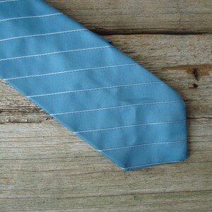 May include: A blue tie with horizontal white stripes. The tie is made of a smooth fabric and has a classic design. The tie is angled across a wooden surface.