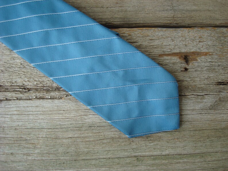 May include: A blue tie with horizontal white stripes. The tie is made of a smooth fabric and has a classic design. The tie is angled across a wooden surface.