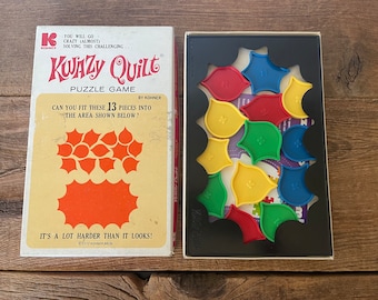 Może przedstawiać: Winietkowa gra planszowa o nazwie "KWAZY Quilt" firmy Kohner. Pudełko zawiera kolorową ilustrację wzoru patchworku i tekst "Czy możesz dopasować te 13 elementów do obszaru pokazanego poniżej?" Gra zawiera 13 kolorowych elementów układanki.